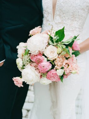Bir gelin düğünde damadının yanında dururken pembe ve beyaz çiçeklerle dolu zarif bir buket tutar..