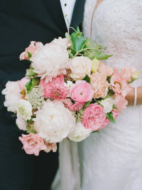 Gelin, düğününde doğal güzelliklerle çevrili çarpıcı bir buket pembe ve beyaz çiçek tutuyor..