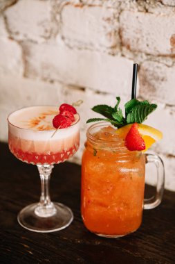 Two vibrant cocktails are presented on a rustic table, showcasing fresh fruits and herbs in a lively bar atmosphere. clipart