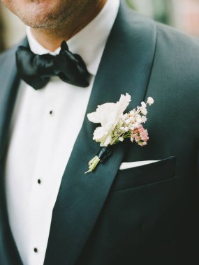 Beyaz gömlekli ve çiçekli bir smokinli bir adam resmi bir etkinlik düzenliyor..