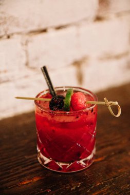 Böğürtlenli ve limonlu renkli bir kokteyl ahşap bir yüzeye oturmuş, canlı renklerini ve süslerini renklendiriyor..