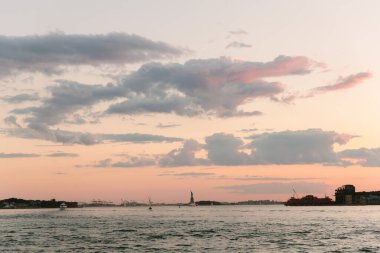 Özgürlük Anıtı güneş batarken dimdik duruyor, New York Limanı 'nın üzerinde canlı renklerle gökyüzünü boyuyor..