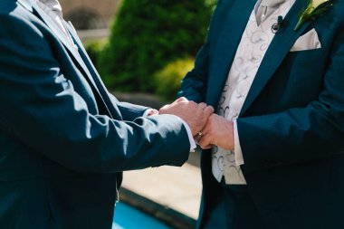 İki adam, yemyeşil yemyeşil bir bahçede el ele tutuşup yüzüklerini değiş tokuş ediyorlar..