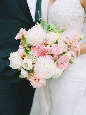 Gelin ve damat, gelin düğün törenlerinde muhteşem bir buket pastel çiçeği tutarken kucaklaşıyor..