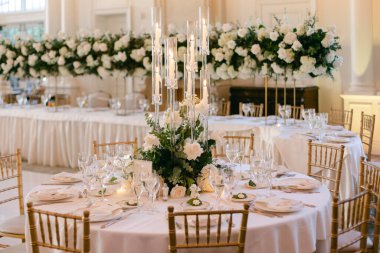 Göz kamaştırıcı bir düğün masası beyaz çiçekler, kristal cam eşyalar ve parlak bir ortamda altın koltuklar..