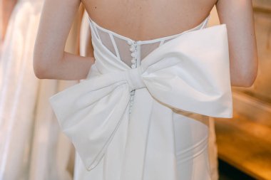 Gelin düğün gününe hazırlanıyor, büyük bir fiyonk ve ince düğmelerle süslenmiş güzel bir elbise sergiliyor..