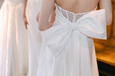 Gelin provası, narin bir fiyonkla süslenmiş ve bir beklenti anı yakalayan çarpıcı bir gelinliği ön plana çıkarıyor..