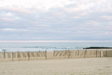 Dalgalar yavaşça kıyıya vururken ahşap çitler günbatımında okyanusun yanındaki kumlu sahili kaplıyor..
