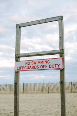 Tahta tabela, alacakaranlıkta sakin bir plajda cankurtaranların izinli olmasından dolayı yüzme yasağı olduğunu gösteriyor..