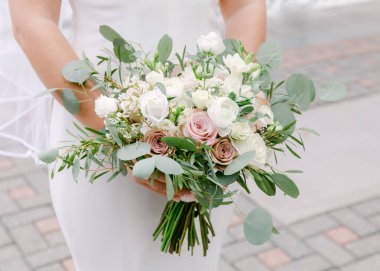 Gelin, güzel bir açık hava ortamında yemyeşil yemyeşil bir buket pembe ve beyaz gül sergiliyor..