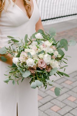 Bir gelin, bir düğün yerinde yemyeşil, beyaz ve pastel güllerden oluşan güzel bir buket tutar..