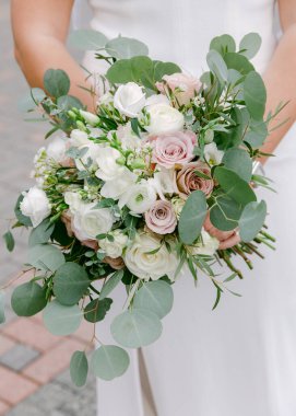 Bir gelin gül, okaliptüs ve diğer narin çiçeklerle dolu bir buket tutar..