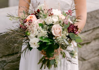 Bir gelin gururla doğanın güzellikleriyle çevrili zarif çiçeklerle dolu buketini sergiler..