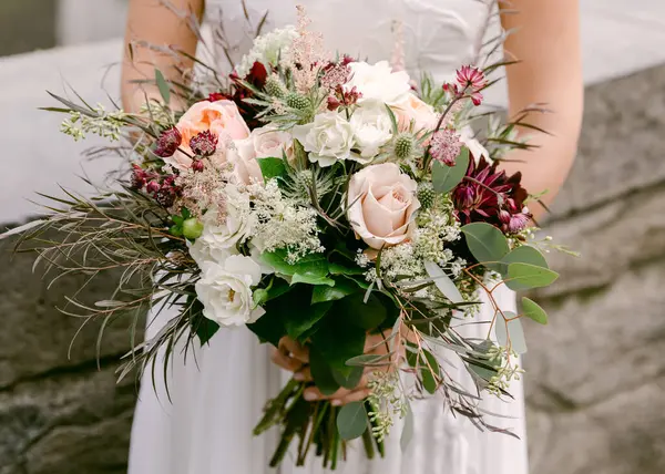 Bir gelin gururla doğanın güzellikleriyle çevrili zarif çiçeklerle dolu buketini sergiler..