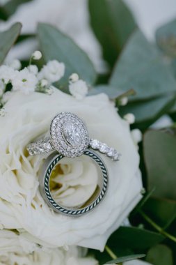Zarif elmas ve gümüş alyanslar beyaz bir çiçeğin üzerinde uzanır. Romantik bir ortamda karmaşık ayrıntıları vurgular..