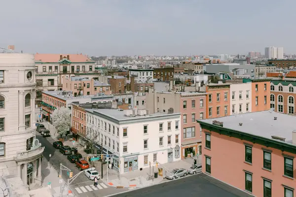 Yaşlı mimari, mavi gökyüzünün altında canlı bir şehir caddesinde ilerleyen insanlar ve arabalarla modern yaşamla karşılaşıyor..