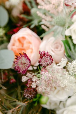 Şeftali güllerinin, beyaz çiçeklerin ve desenli yeşilliğin taze bir karışımı büyüleyici bir ortamda doğal bir zarafet yayar..