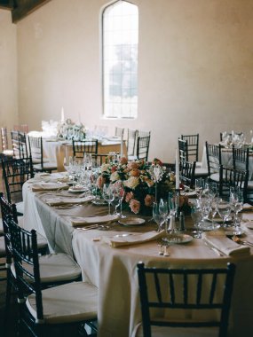 Güzel düzenlenmiş bir yemek masasında bardaklar, tabaklar ve büyüleyici bir mekanda canlı bir çiçek süsü var..