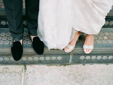 Parlak sandaletli gelin ve siyah ayakkabılı damat düğün günü neşe saçan açık hava basamaklarında yan yana dururlar..