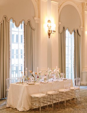 Sofistike bir salonda güzel düzenlenmiş bir yemek masası. Zarif çiçekli süsler ve yumuşak mum ışığında..