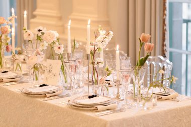 Güzel düzenlenmiş bir yemek masasında şık bir mekanda zarif bir toplantı için mumlar ve taze çiçekler sergilenir..