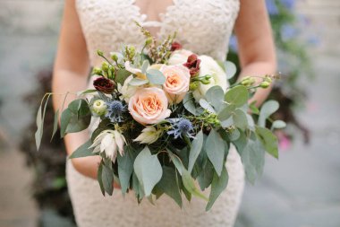 Dantelli gelinlik giymiş bir gelin, gül buketini açık havada sergiliyor..