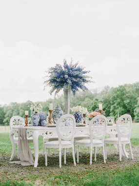 Yeşilliklerle çevrili beyaz sandalyeli ve vazolu güzel bir masa, güzel bir toplantı için hazır..
