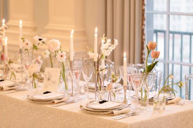 Güzel düzenlenmiş bir yemek masasında özel bir durum için zarif cam eşyalar, mumlar ve taze çiçekler bulunur..