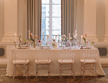 Güzel düzenlenmiş bir yemek masasında zarif çiçekli süsler ve sofistike bir ortamda mum ışığı bulunur..