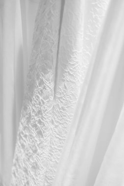 Narin beyaz kumaş nazikçe kıvrılır ve hafif aydınlatma alanına huzur veren bir dokunuş eklenir..