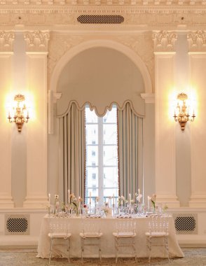 Zarif bir şekilde hazırlanmış bir yemek masası sofistike bir salonda, hafif ışıklandırma ve dekorasyon içeriyor..