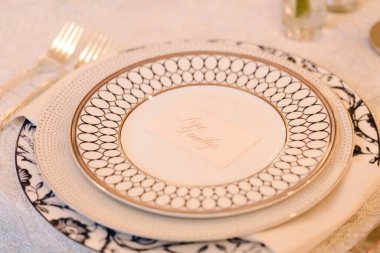 Güzel düzenlenmiş bir yemek masasında zarif tabaklar ve bir isim kartı bulunur. Şenlikli bir yemek için zarafet sergilenir..