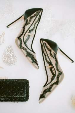Dantel ve süslerle süslenmiş şık topuklu ayakkabılar, özel etkinlikler veya partiler için dekoratif aksesuarlarla çevrili düz bir yüzeyde zarif bir şekilde otururlar..