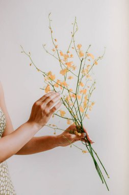 Bir kadın nazikçe bir buket narin sarı çiçek tutar ve düzenler. İçerde huzurlu bir atmosfer yaratır..