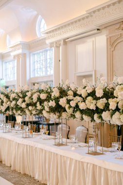 Uzun çiçek süslemeleri olan güzel bir masa büyük salonda nefes kesici bir atmosfer yaratıyor..