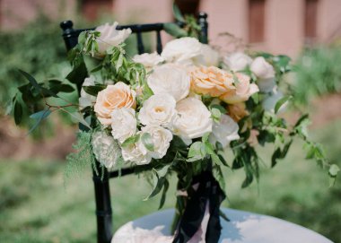 Beyaz ve şeftali güllerinden oluşan büyüleyici bir buket canlı bir bahçede bir sandalyenin üzerinde duruyor. Düzen yemyeşil, güzelliğini ve çekiciliğini arttırıyor..