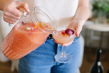 Bir insan narin bir bardağa canlı bir içki doldurur. Sıcak bir toplantıda çiçek süsleri sergiler..