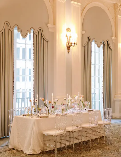 Sofistike bir salonda güzel düzenlenmiş bir yemek masası. Zarif çiçekli süsler ve yumuşak mum ışığında..