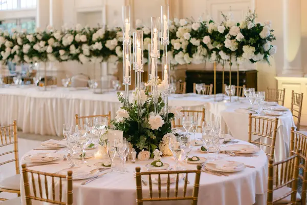 Göz kamaştırıcı bir düğün masası beyaz çiçekler, kristal cam eşyalar ve parlak bir ortamda altın koltuklar..
