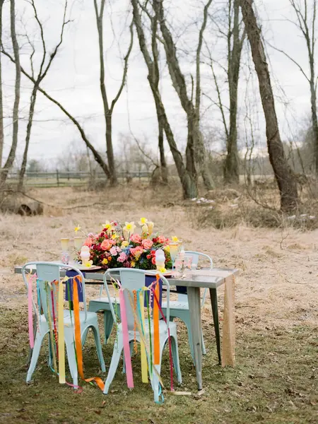 Çok güzel düzenlenmiş bir açık masa canlı çiçekler ve sandalyelere takılmış renkli kurdeleler sergiliyor. Bu düzen, misafirleri doğadaki bahar toplantısının tadını çıkarmaya davet ediyor..