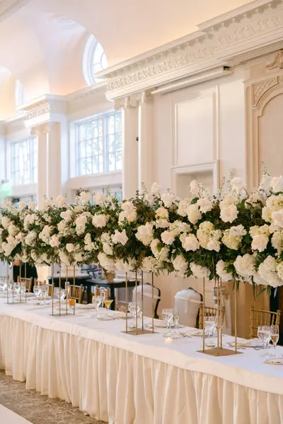 Uzun çiçek süslemeleri olan güzel bir masa büyük salonda nefes kesici bir atmosfer yaratıyor..