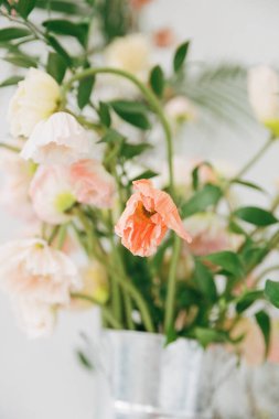 Parlak vazodaki yumuşak pastel çiçeklerden oluşan bir buket, doğal ışıkla aydınlanan bir iç mekan ortamını aydınlatır..