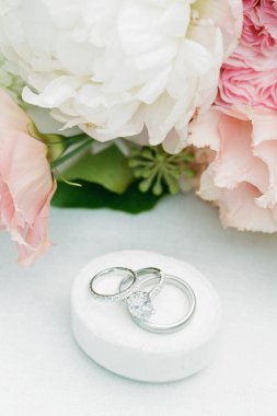 Güzel alyanslar romantik bir yerde pembe ve beyaz çiçeklerle süslenmiş bir mindere otururlar..