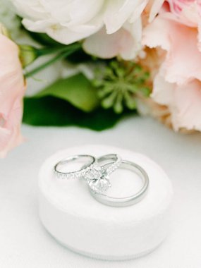 Yumuşak çiçek aranjmanlarıyla yastıklı bir yüzeyde duran alyansları kapatın, bir aşk anı yakalayın.