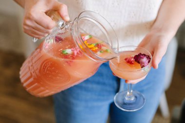 Bir insan zarif bir bardağa çiçeklerle doldurulmuş canlı bir meyve suyu dökerek nefis bir ferahlatıcı oluşturur..