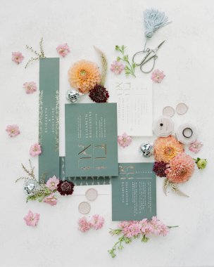 Hassas düğün davetiyeleri sanatsal olarak küçük çiçekler, el işi aletleri ve dekoratif aksanlarla düzenlenir. Bu yaratıcı görüntü zarif tasarımı ve doğal elementleri vurgular..