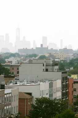 Binalar ve çatılar ön planda dururken, şehrin silueti arka plandaki sisin içinde kayboluyor..