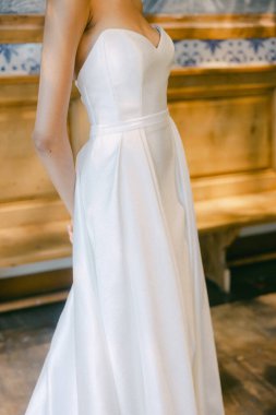 Pürüzsüz, beyaz bir gelinliğin yakın plan görüntüsü tasarım detaylarını ev ortamında vurguluyor..