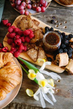 Çeşitli taze meyveler ve fırınlanmış eşyalar ahşap bir masanın üzerine güzelce serilmiş, herkesi eğlenmeye davet ediyor..
