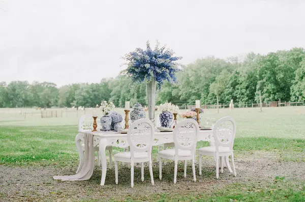 Bulutlu bir günde manzaralı yeşil bir alanda beyaz sandalyeli ve çiçekli güzel bir masa..